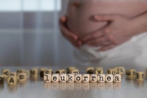 Слово лейкорея, состоящее из деревянных букв. Беременный человек на заднем плане